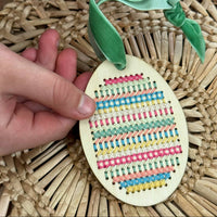 Decorative Easter egg with colorful patterns and a green ribbon held by hands on a woven mat.