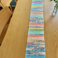 Colorful woven table runner on a wooden table with a plant in the background