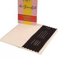 A vintage-style sewing needle case and box set on a plain white background. The box is pink with a yellow vertical stripe, a red circle, and an illustration of a woman holding needles, with the text 'le Zaùfil' and 'Aiguilles Perles.