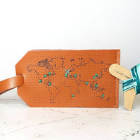 Brown leather luggage tag with world map design on a light surface.