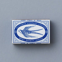 A vintage matchbox for 'Waltorine Company Limited' featuring a blue swallow design on a white background, set against a solid gray backdrop.