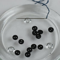 Black buttons on a glass plate with a needle and thread.