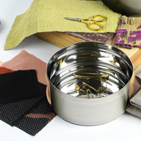 Metal container on a colorful fabric background with scissors and other items.
