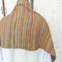 Colorful striped shawl draped over a mannequin against a floral wallpaper background.