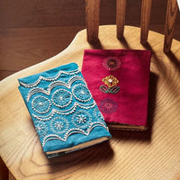 Embroidered fabric samples on a wooden chair with a magazine open to pages showing similar designs.