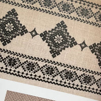 Textile with black geometric patterns on a fabric swatch and design diagram in a book.