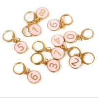 Pink number charms with gold rings on a white background