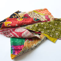 Assorted colorful kantha fabric scraps with large stitches, laid out on a white surface.