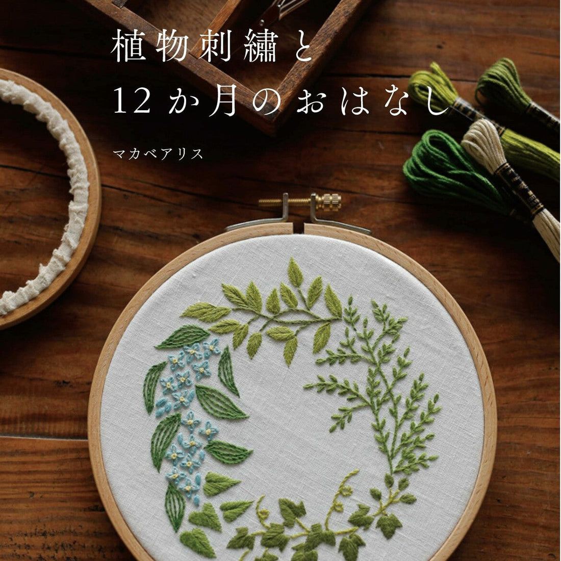 Embroidery hoop with floral design on a wooden surface, surrounded by embroidery tools.