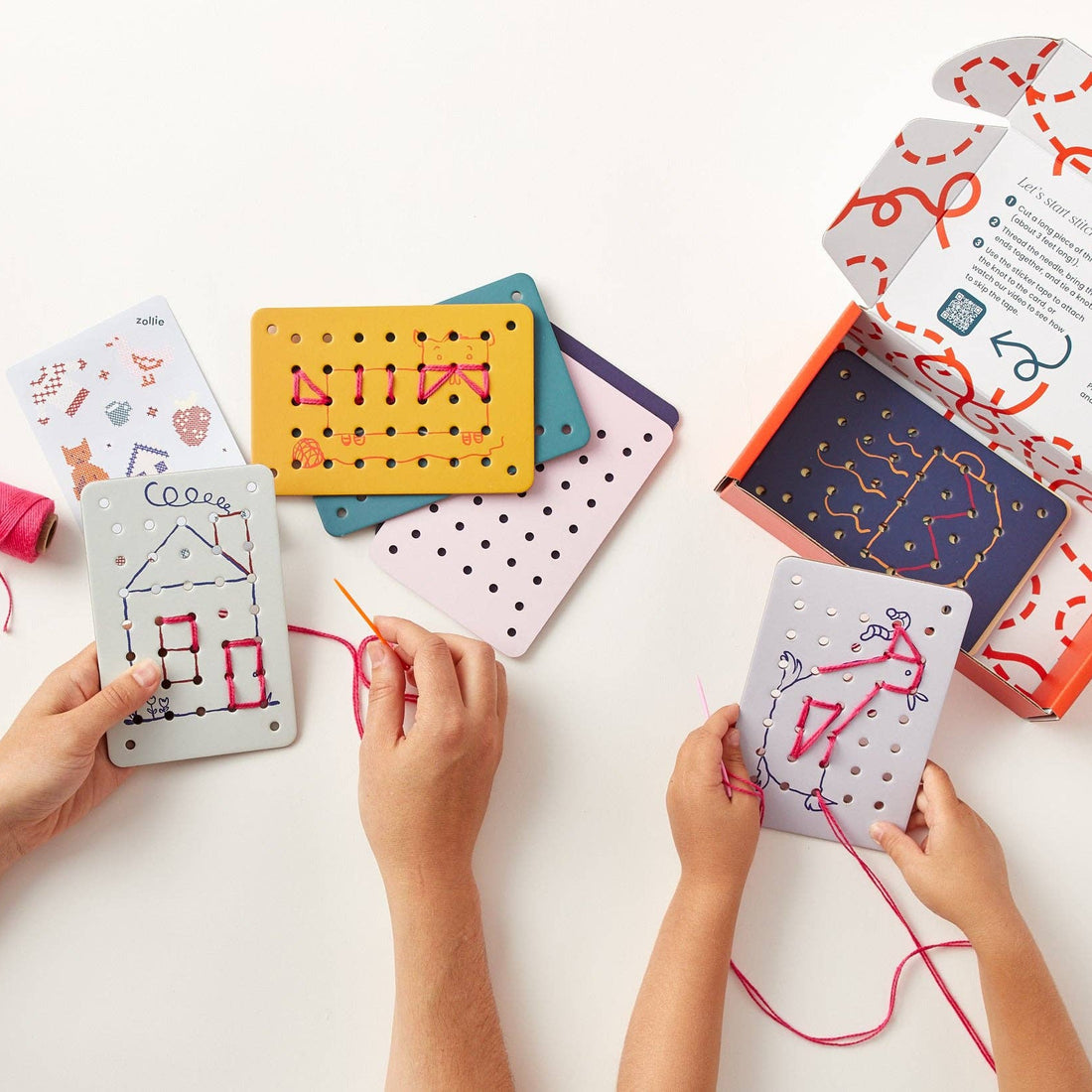 Children's hands working on a craft project with colorful cards and thread on a white surface.