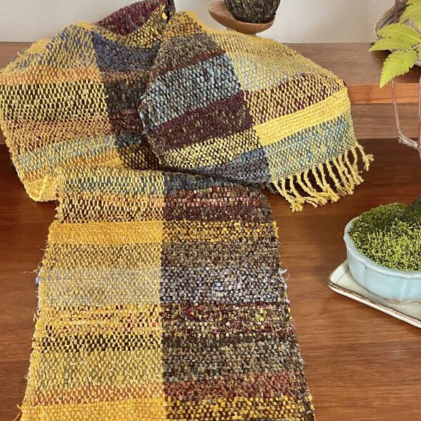 Multicolored woven scarf on a wooden surface with a small potted plant.
