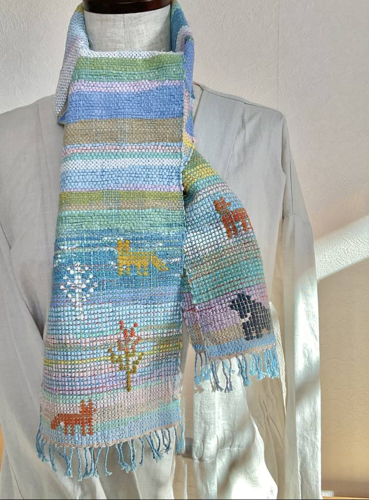 Colorful woven scarf with animal designs on a mannequin against a neutral background