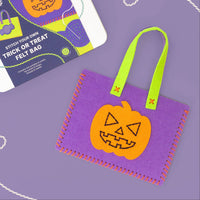 A Halloween-themed felt bag kit shown with its printed packaging box on a lavender background. The kit includes a purple felt bag with a stitched orange jack-o'-lantern patch and bright green handles, alongside the box labeled 'Stitch Your Own Trick or Treat felt bag'.