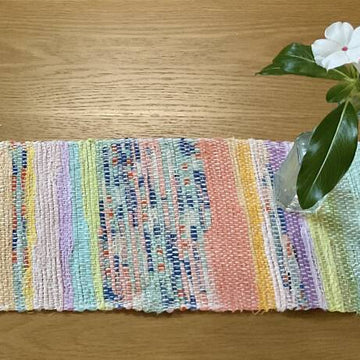 Colorful woven mat on a wooden surface with a small plant.