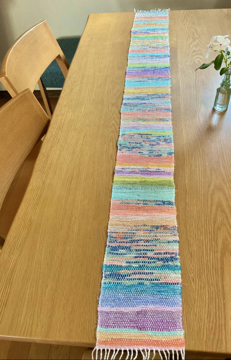 Colorful woven table runner on a wooden table with a plant in the background