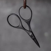 Pair of black-handled scissors hanging on a hook against a gray background