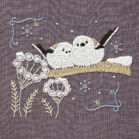 Embroidered design of two birds on a branch with flowers and snowflakes on a textured fabric background.