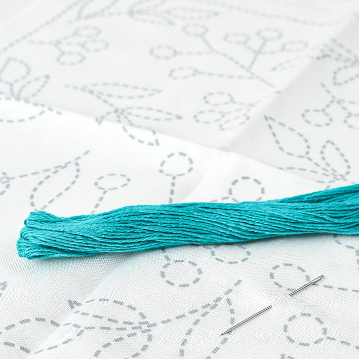 Turquoise embroidery floss and needle on a white fabric with embroidery patterns