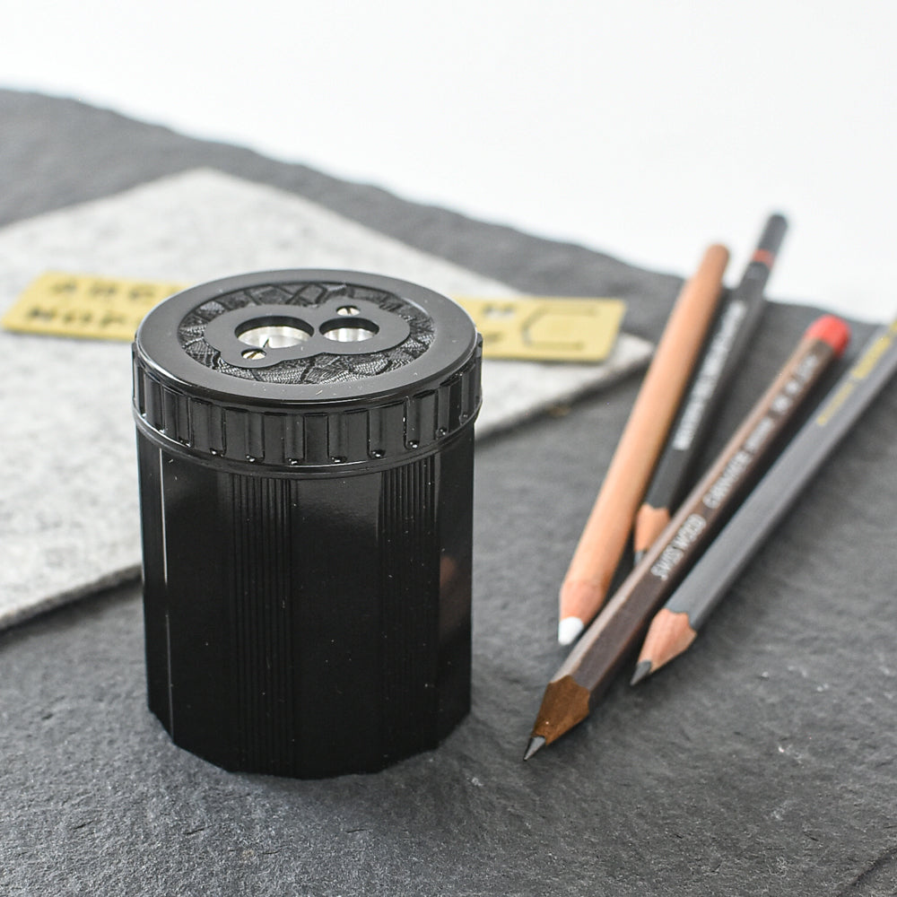 Black pencil sharpener with sharpened pencils on a gray surface