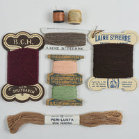 A flat lay of vintage sewing and embroidery threads on a white background, including spools and a skein of Peri-Lusta spun mending thread. Visible brands include B.