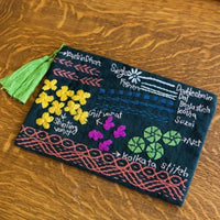 Embroidered pouch with floral designs and text on a wooden surface