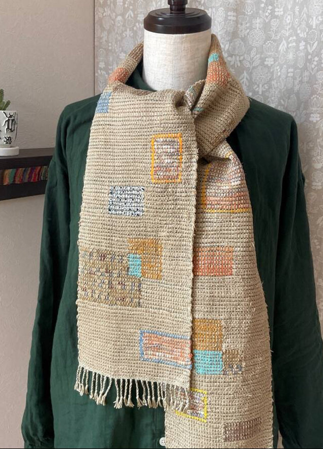 Textile scarf with geometric pattern draped over a green garment, close-up on fabric texture.