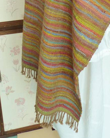 Multicolored striped shawl on a mannequin against a floral wallpapered wall.