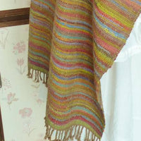 Multicolored striped shawl on a mannequin against a floral wallpapered wall.