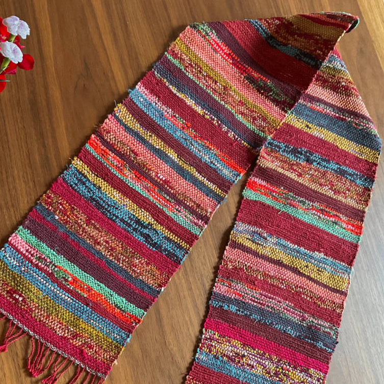 Multicolored striped scarf on a wooden surface with flowers in the background