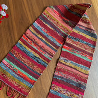 Multicolored striped scarf on a wooden surface with flowers in the background