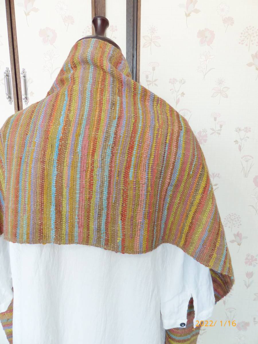 Colorful striped shawl draped over a mannequin against a floral wallpaper background.