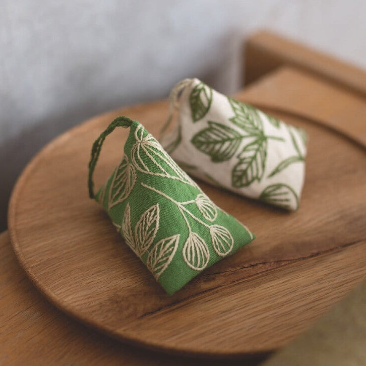 Two small fabric pouches with leaf patterns on a wooden tray.