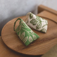 Two small fabric pouches with leaf patterns on a wooden tray.