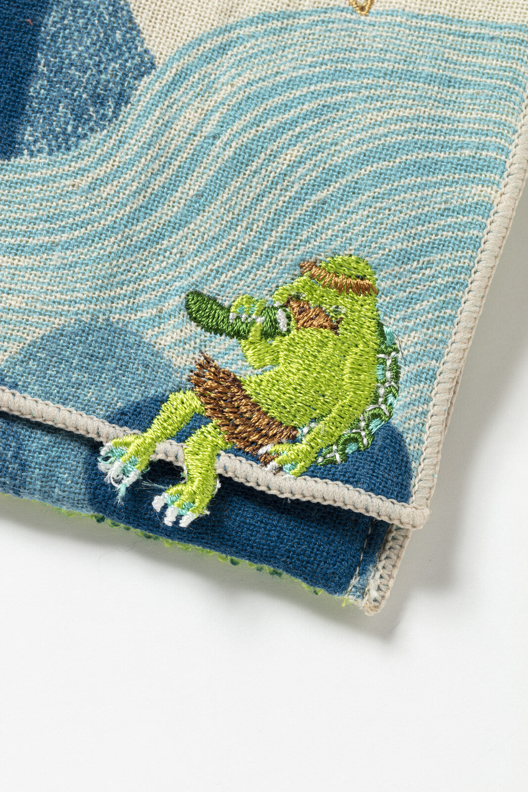 Embroidered green frog on a textured blue and white fabric