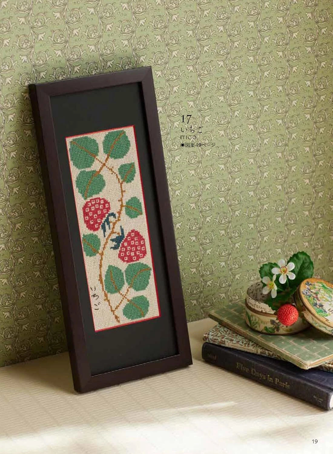 Framed cross-stitched pattern of berries and leaves on a textured green wall.