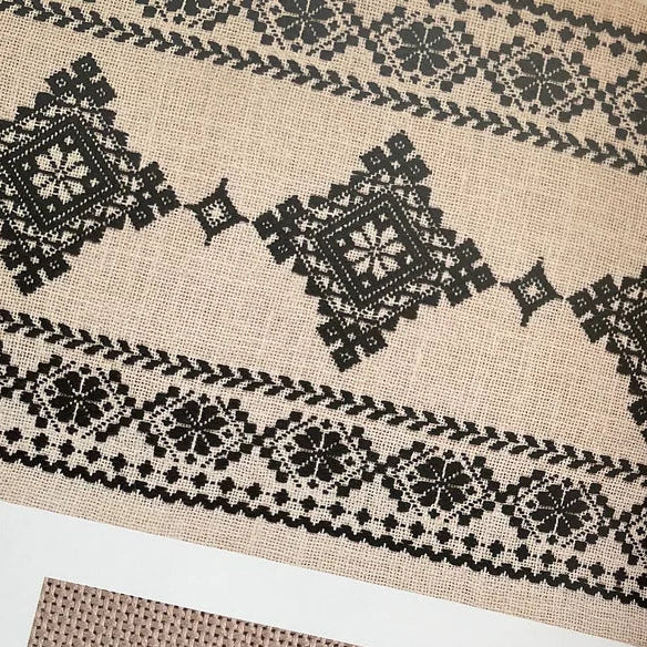 Textile with black geometric patterns on a fabric swatch and design diagram in a book.