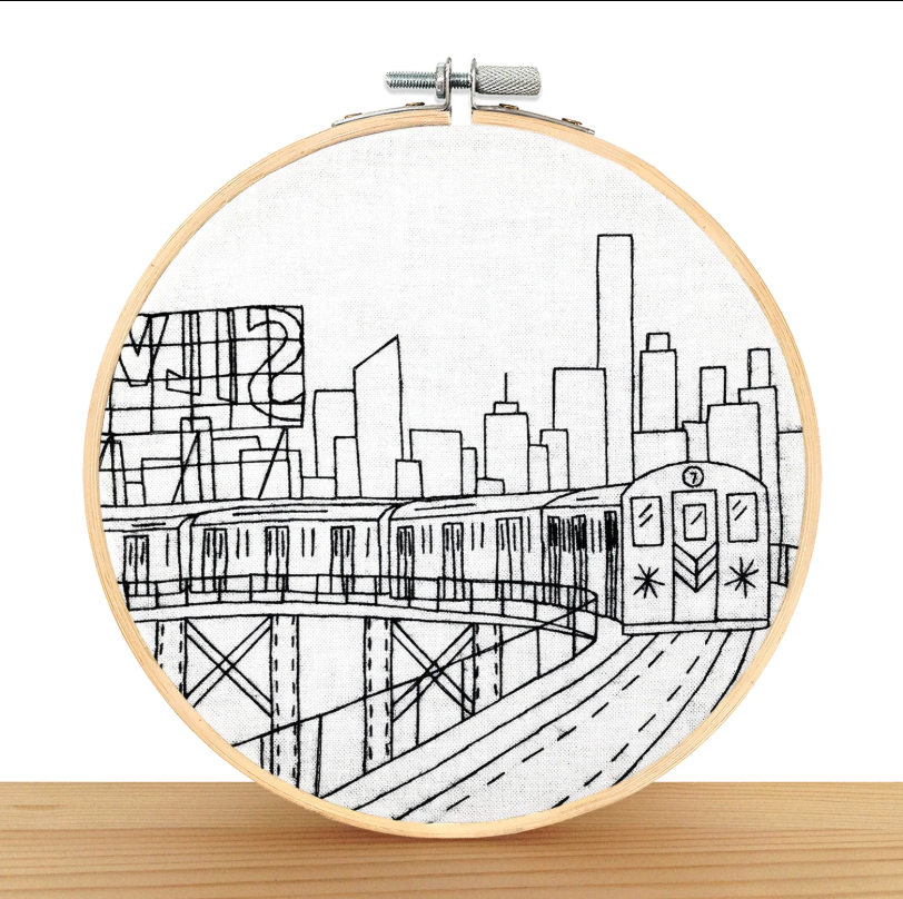 Embroidery hoop with a black and white cityscape design featuring a train.