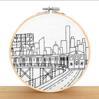 Embroidery hoop with a black and white cityscape design featuring a train.