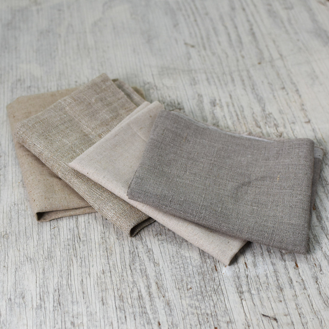 four pieces of folded natural brown linen fabric laid out in a fan shape to show variations in the colors and textures of each.