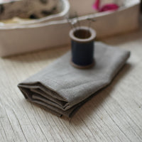 a piece of natural brown linen fabric, folded, with a blue-glazed ceramic spool pin holder in the background.